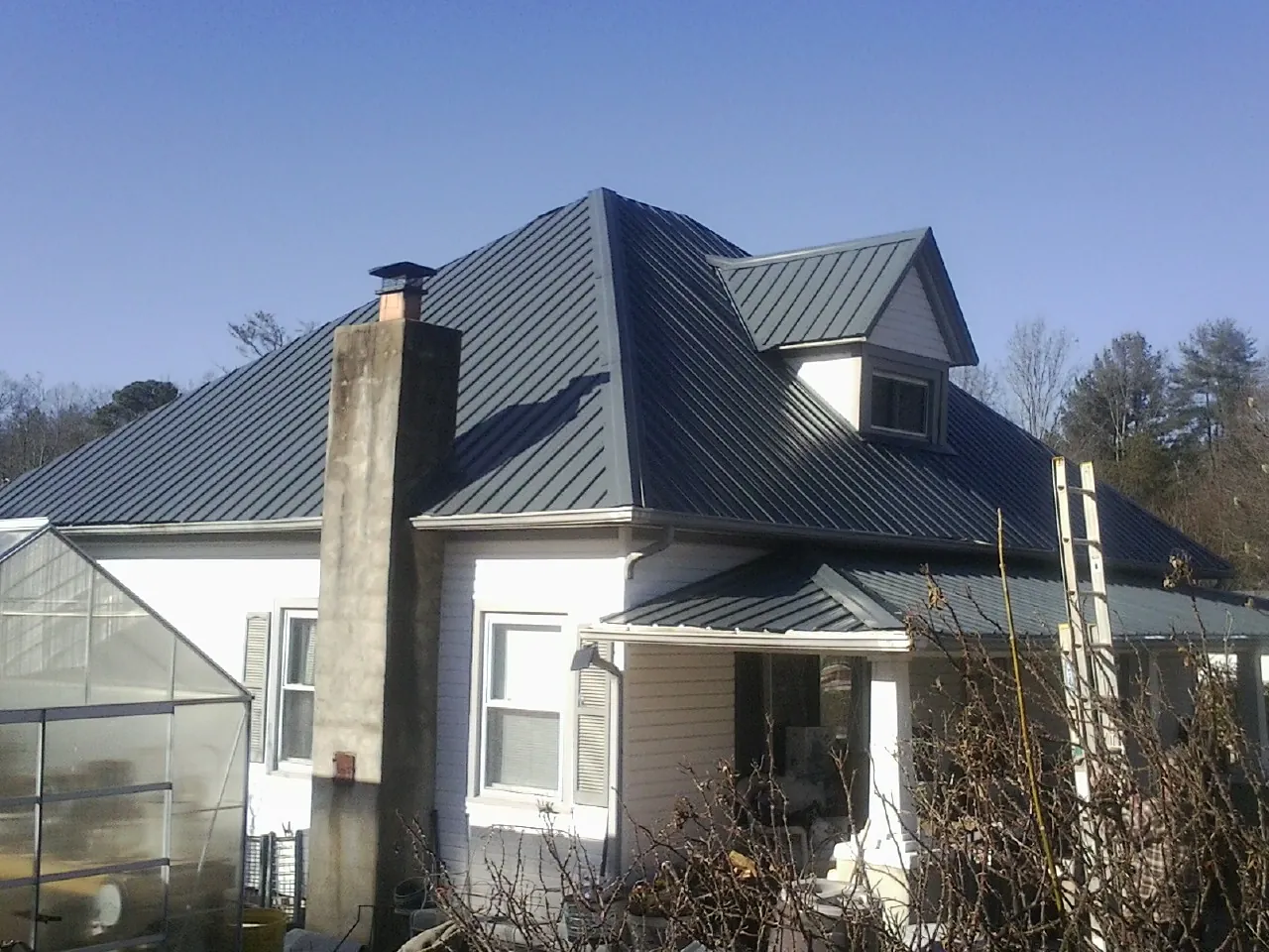 Dark blue standing seam metal roof on a white farmhouse with dormer — Slate & Tile Roof Repair by Roofing Brothers in Jenners