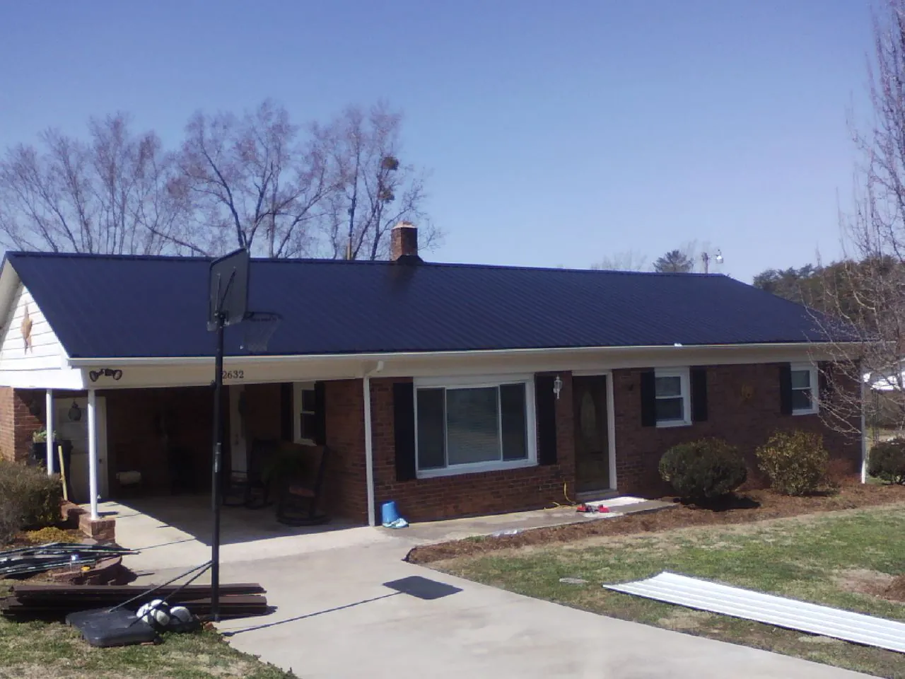 Finished dark blue metal roof on a brick ranch with a carport in Jenners