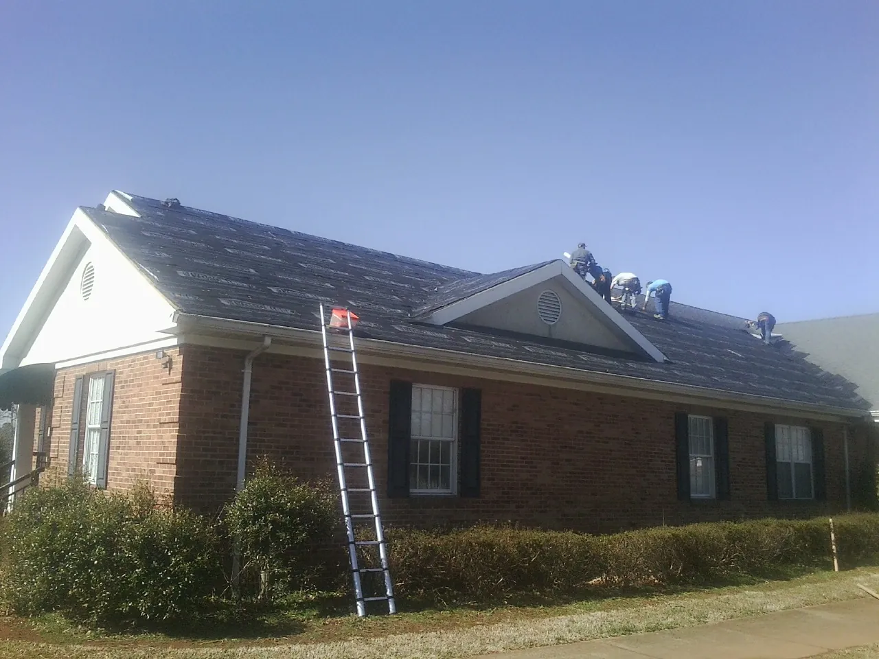 Crew tearing shingles off a brick ranch roof with a ladder set — Metal Roof Repair work by our crew in Jenners