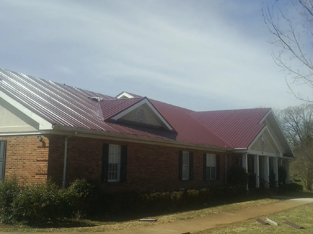 Red metal roof with gabled entries on a long brick building, from a Hail Damage Roof Repair job in Jenners