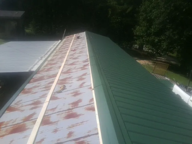 Old rusted panels beside newly installed green metal roofing — Wind Damage Roof Repair by Roofing Brothers in Jenners