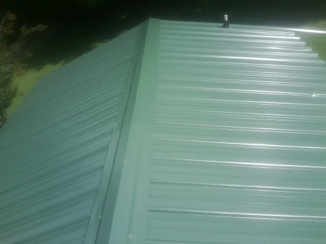 New green metal panels meeting at the ridge of a roof — Flat Roof Repair work by our crew in Jenners