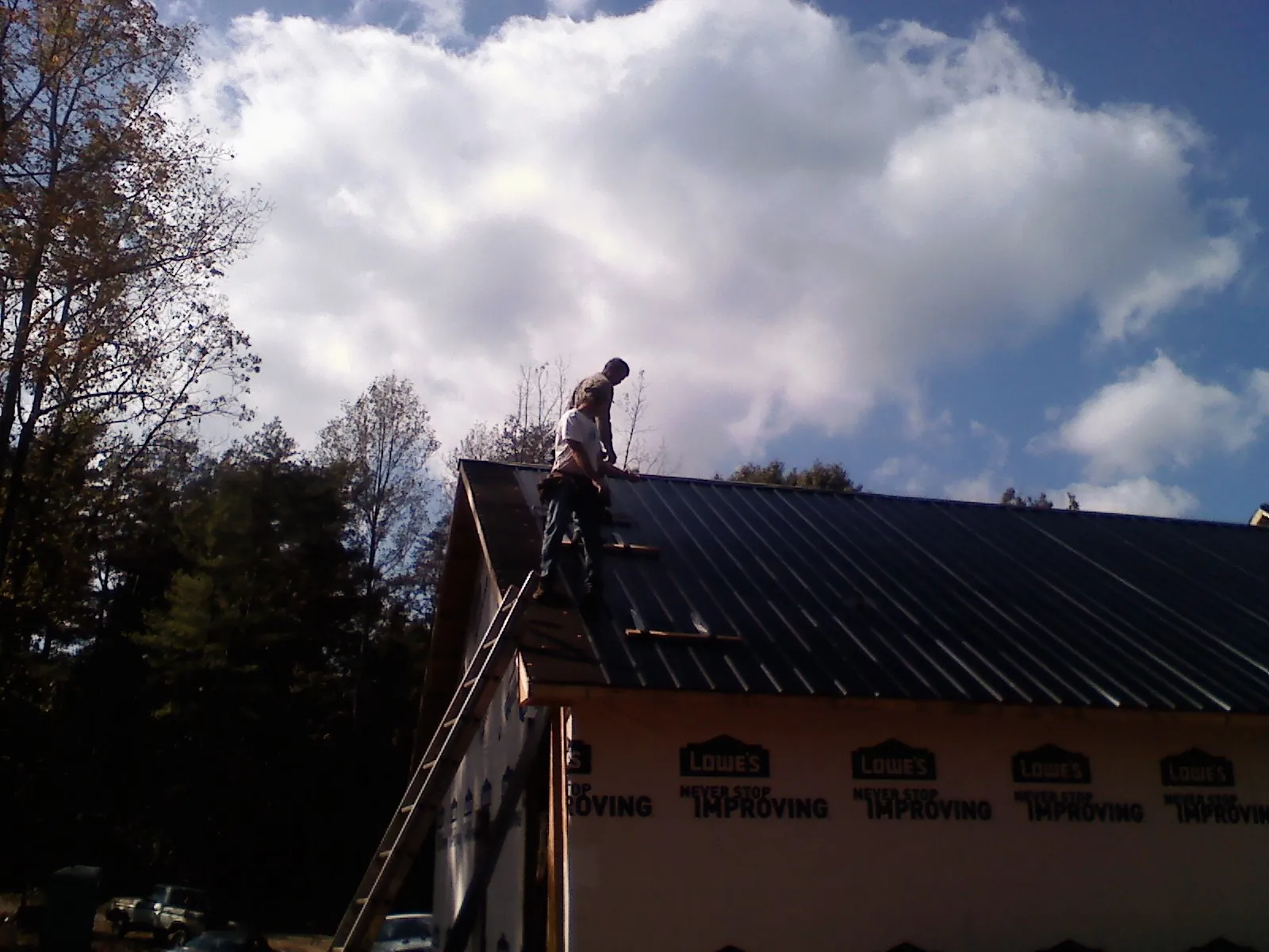 Roofer fastening dark metal panels high against a cloudy sky, from a Roof Inspection job in Jenners