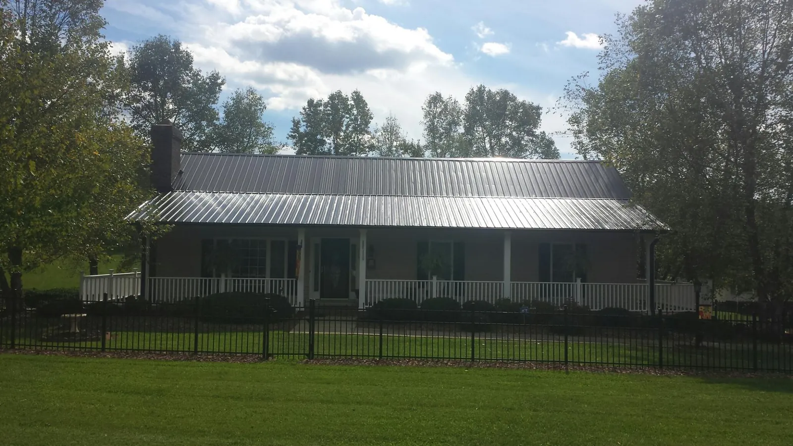 Gray metal roof on a brick ranch with a full width front porch — Gutter Guard Installation work by our crew in Jenners