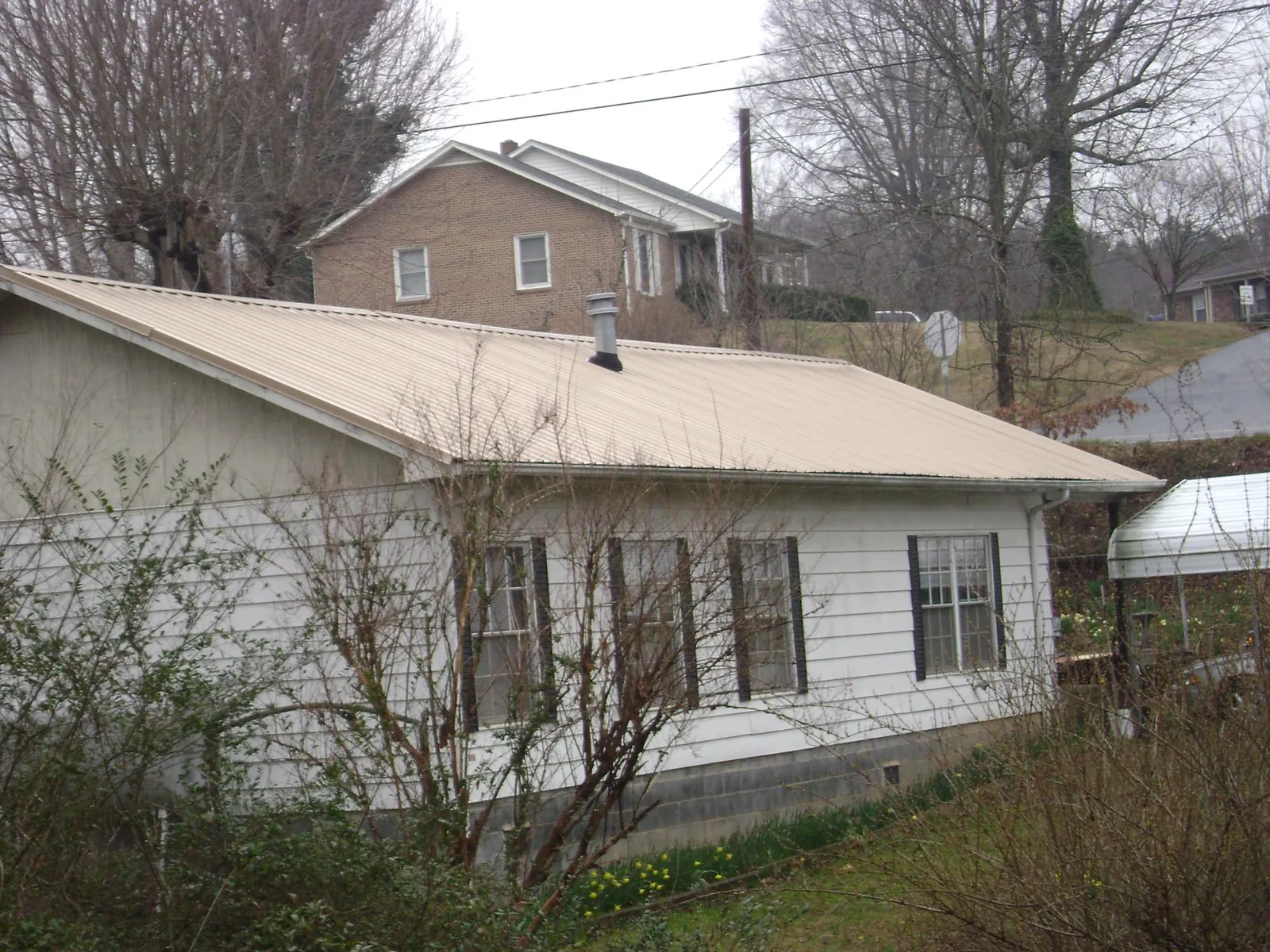 Tan metal roof on a white sided house set into a hillside — Commercial Roofing by Roofing Brothers in Jenners