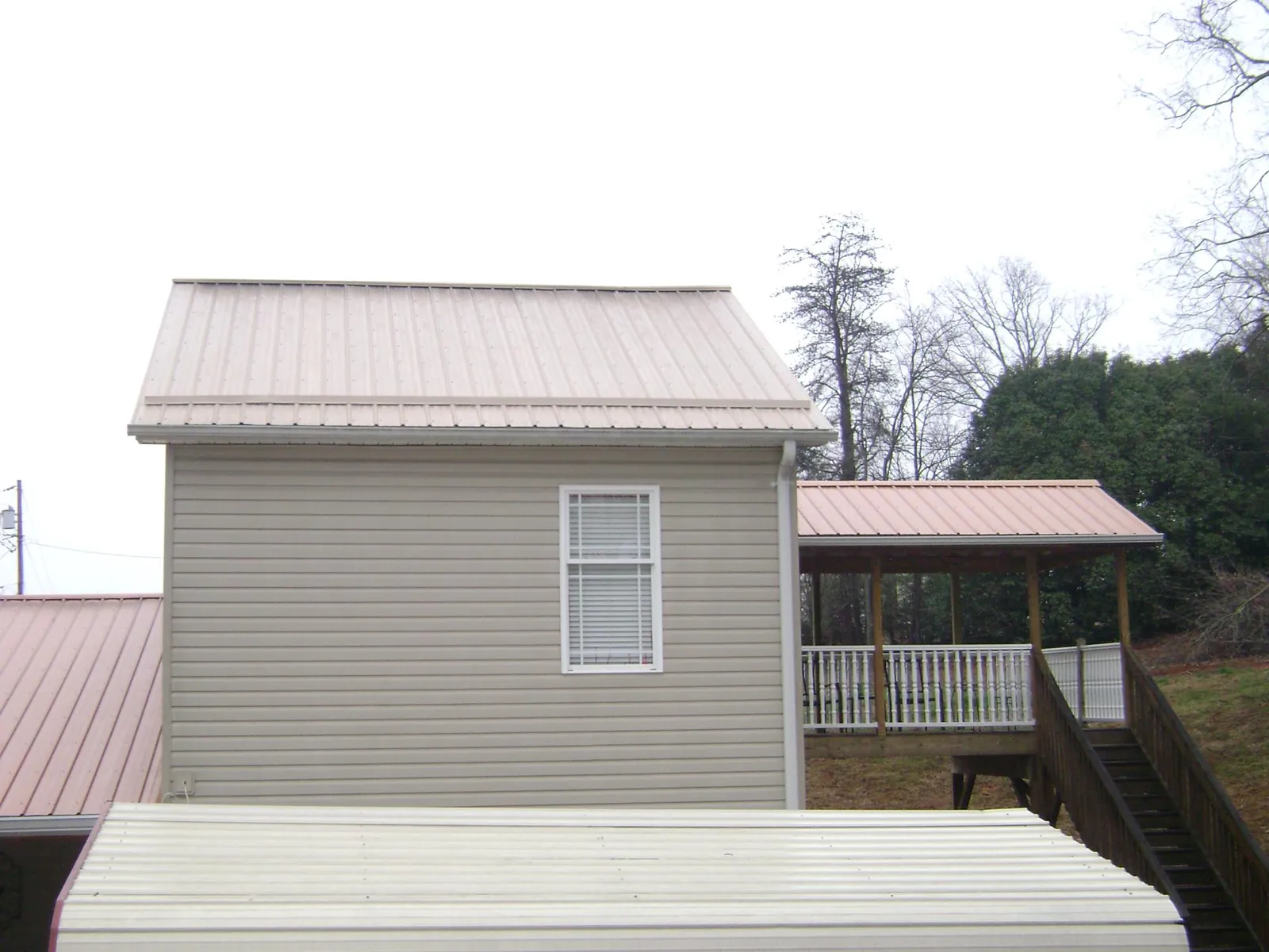 Tan metal roofs on a two story addition and attached porch, from a Roof Replacement job in Jenners